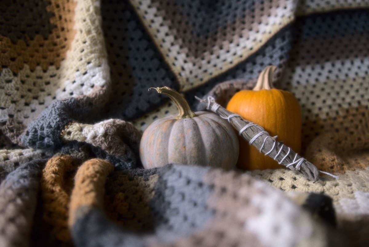 A cream and grey granny square crochet blanket with two mini pumpkins