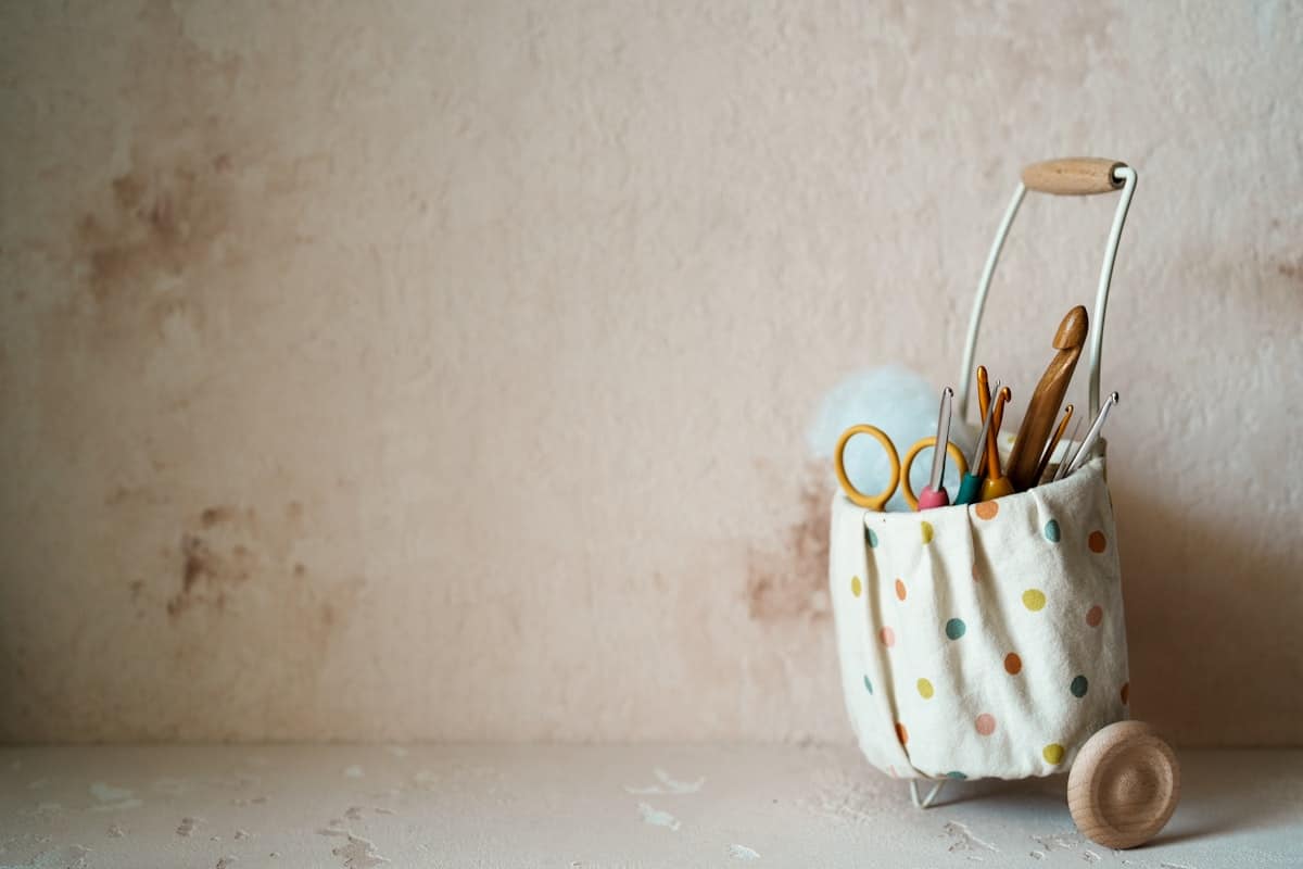 A polka dot fabric caddy holding crochet hooks and scissors against a warm terracotta wall